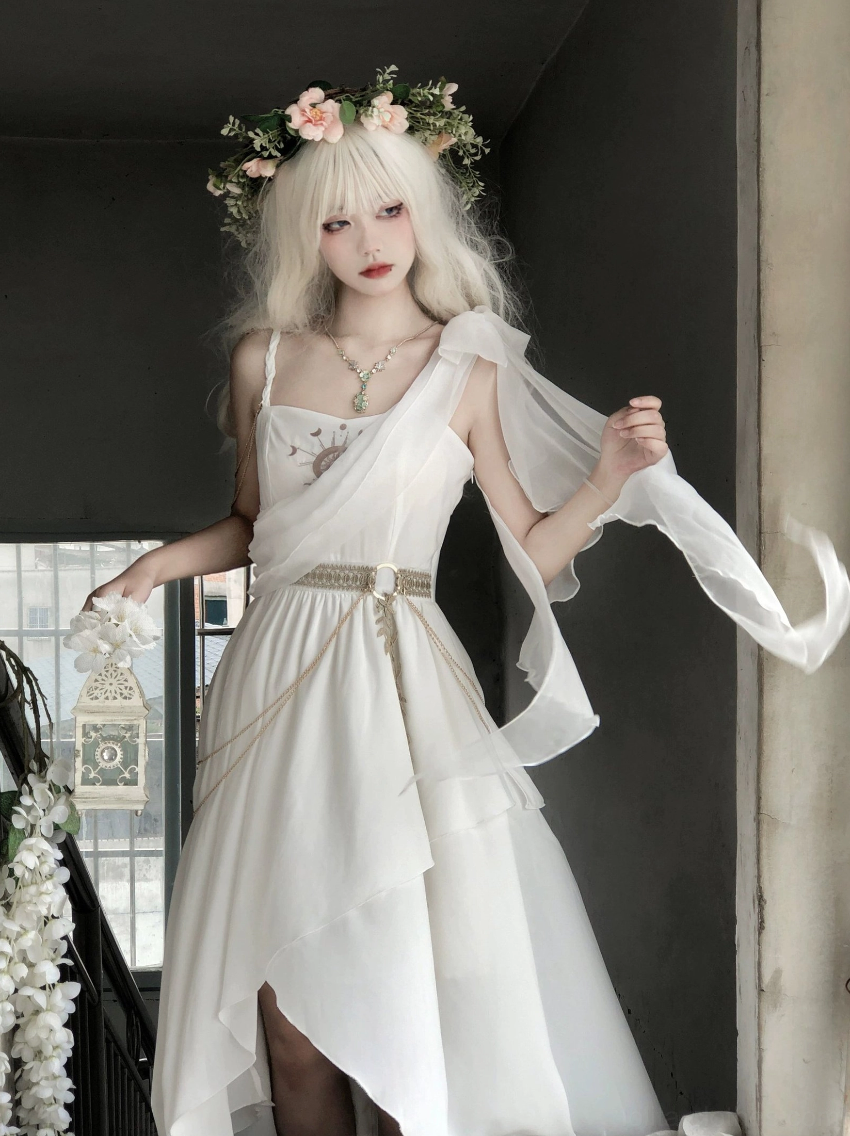 Tethys Tears Greek style white chiffon JSK dress full front three-quarter view on flower crown model showing flowy chiffon drape uneven hem layered necklace bracelet white flower garland accessories