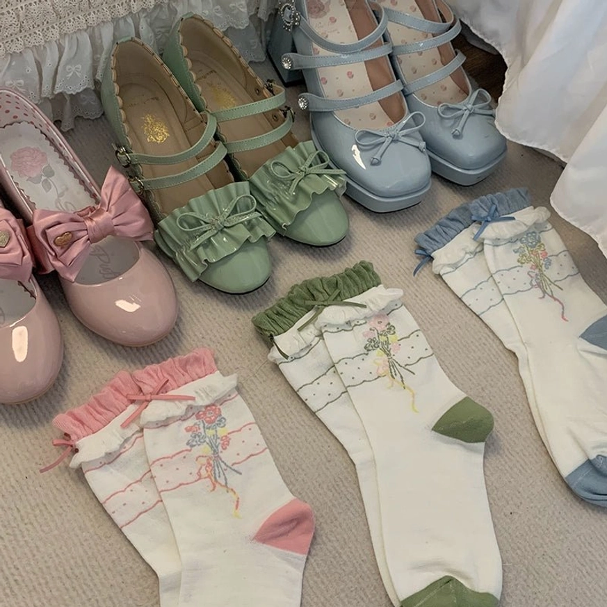 Flat lay top-down view of three color variants of lolita ankle socks with matching Mary Jane shoes all featuring floral prints and ruffled cuffs in blue pink and green
