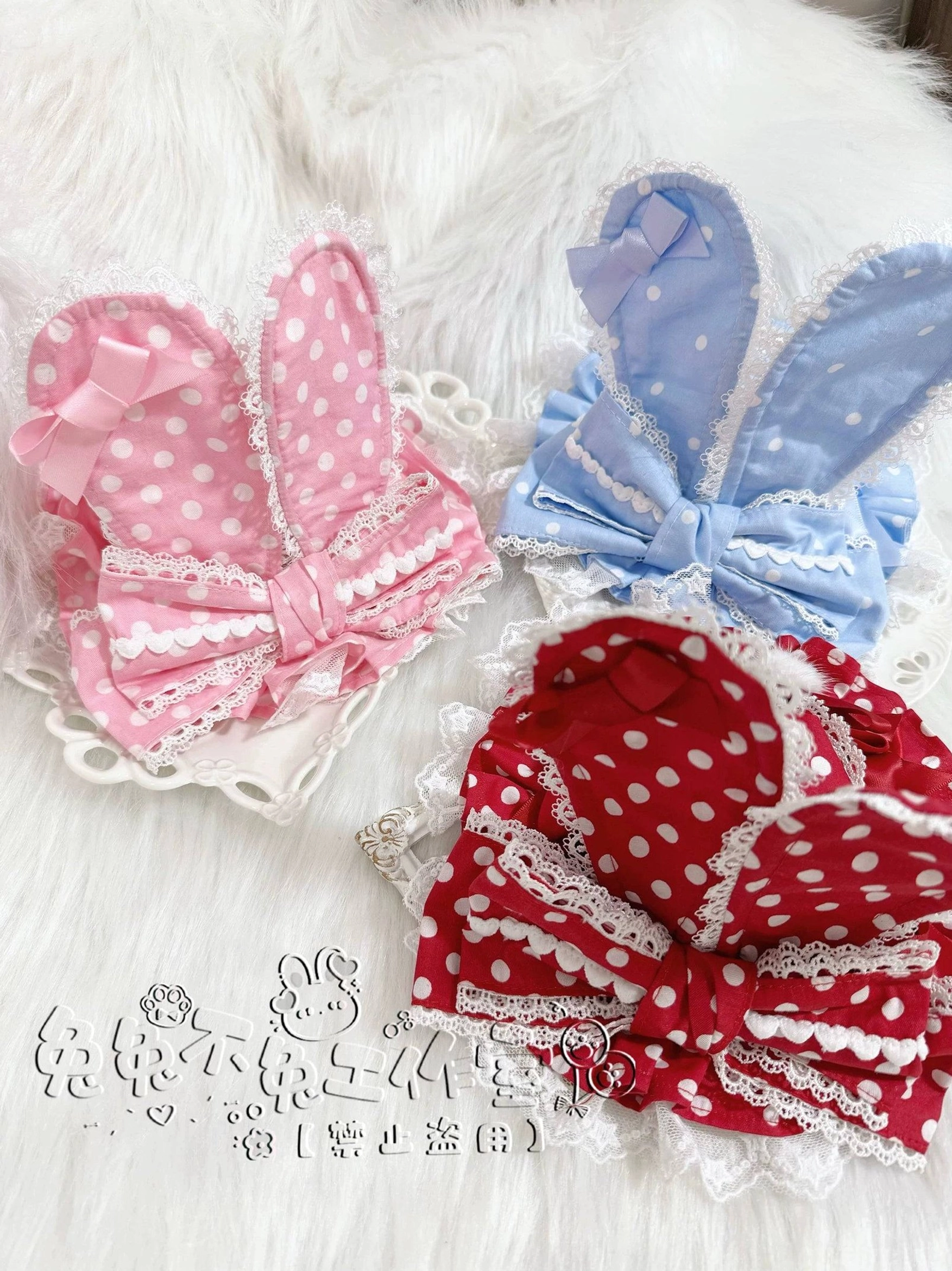 Three Lolita bunny ear hair accessory styles pink polka dot blue satin red polka dot with ribbon bows lace trim and pom-pom decorations flat lay display