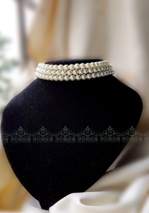 Slim three-row white pearl choker front view on black velvet neck mannequin, displaying compact round pearl construction and neat layered stacked design
