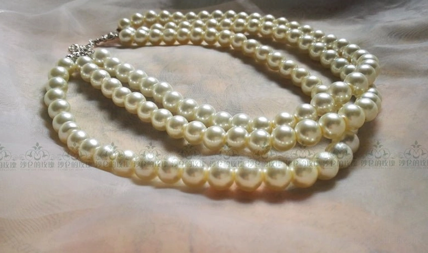 Three-strand pearl choker necklace flat lay on textured fabric backdrop, showing slightly graduated pearl sizes across layers with silver hardware closure
