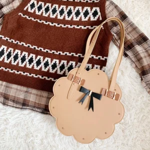 Kawaii toffee cookie Lolita handbag displayed from above beside vintage jacquard knitwear on soft white fabric
