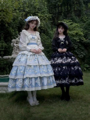 Twin classic lolita JSK outfits side-by-side with coordinating bonnets displayed outdoors by decorative stone fountain
