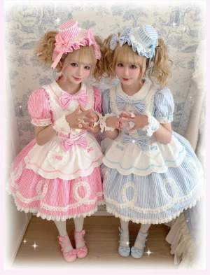 Two female models wearing matching pink and blue striped old school lolita OP dresses with twin tail hairstyles and matching bonnets in vintage floral interior