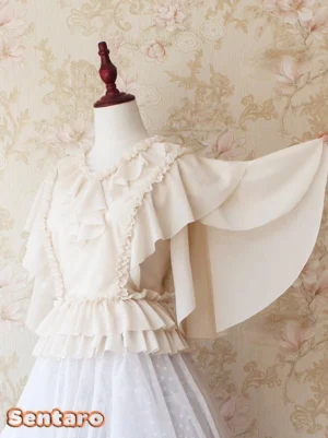 Cream apricot V-neck ruffled Lolita blouse with ethereal flutter sleeves displayed on dress form from front three-quarter angle, paired with white tulle skirt against vintage floral backdrop