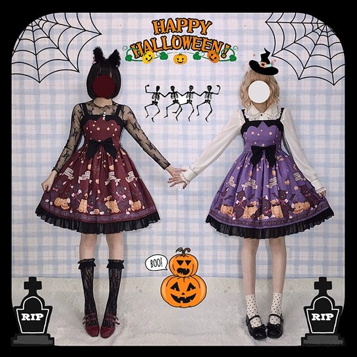 Full body side view of wine red and purple Halloween themed lolita jumper skirt with vampire cat and pumpkin patterns matching cat ear hair accessories on Halloween backdrop with spider webs and tombstones