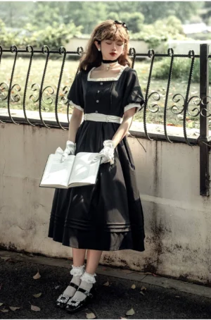 Vintage black square neckline Lolita OP dress full front view worn by model in outdoor vintage setting with iron fence backdrop, showcasing short puff sleeves and white ruffled lace contrast trims