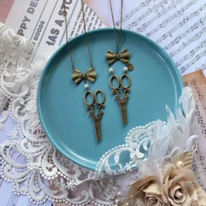 Vintage bow-scissors shaped Lolita sweater chain necklace displayed on blue ceramic tray with lace doily, featuring antique bronze bow pendant, pearl accents and scissor charm in flat lay composition
