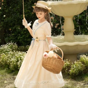 Full-body outdoor view of model wearing cream-colored vintage Lolita one-piece dress with straw boater hat, short puff sleeves, lace trims, blue waist sash with floral ornament, carrying wicker picnic basket in courtyard with stone fountain