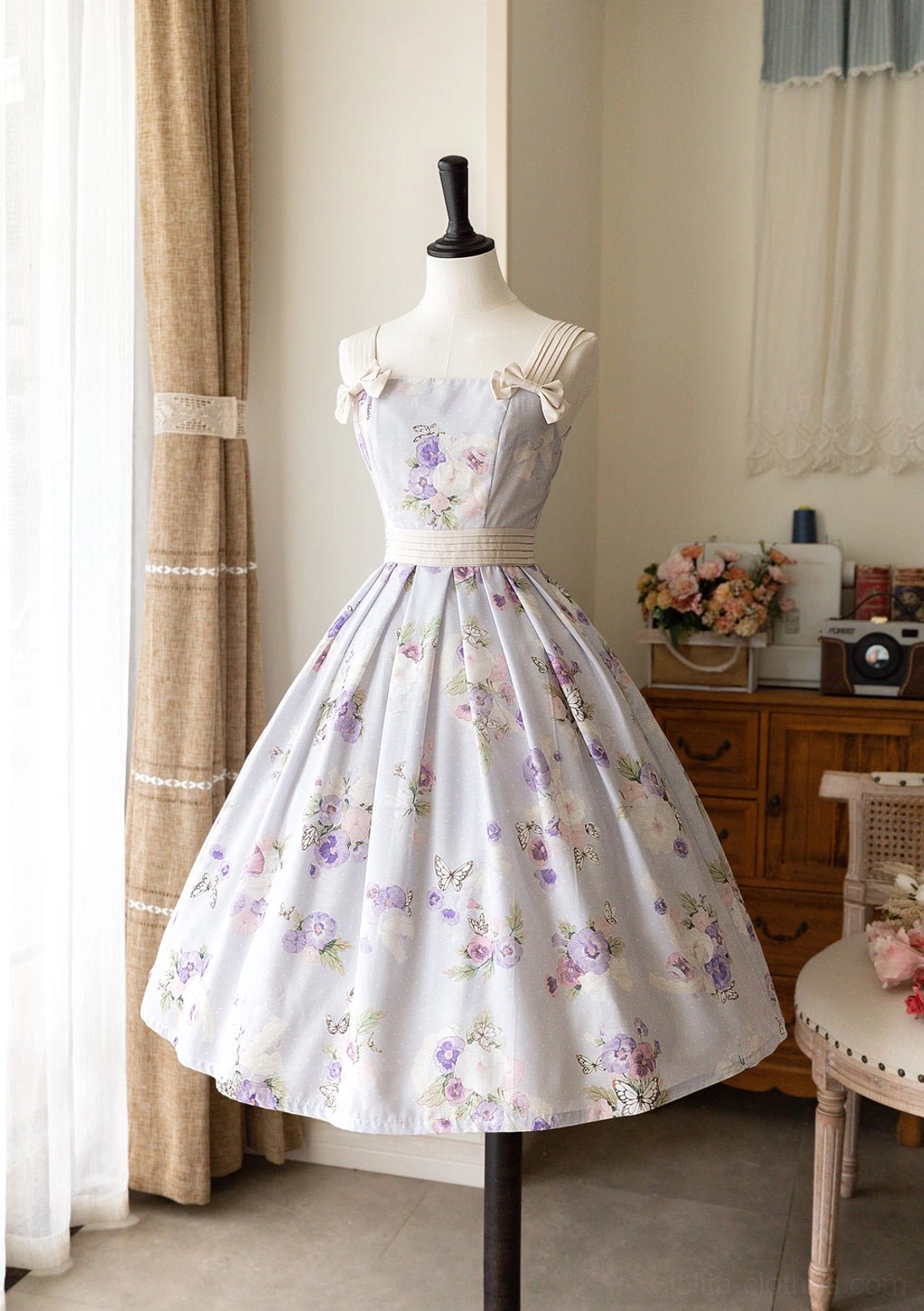 Cream-based floral lolita JSK dress with violet and purple flower prints, coordinating purple waist sash, shoulder bow details, and voluminous flared midi silhouette shown from positive front angle