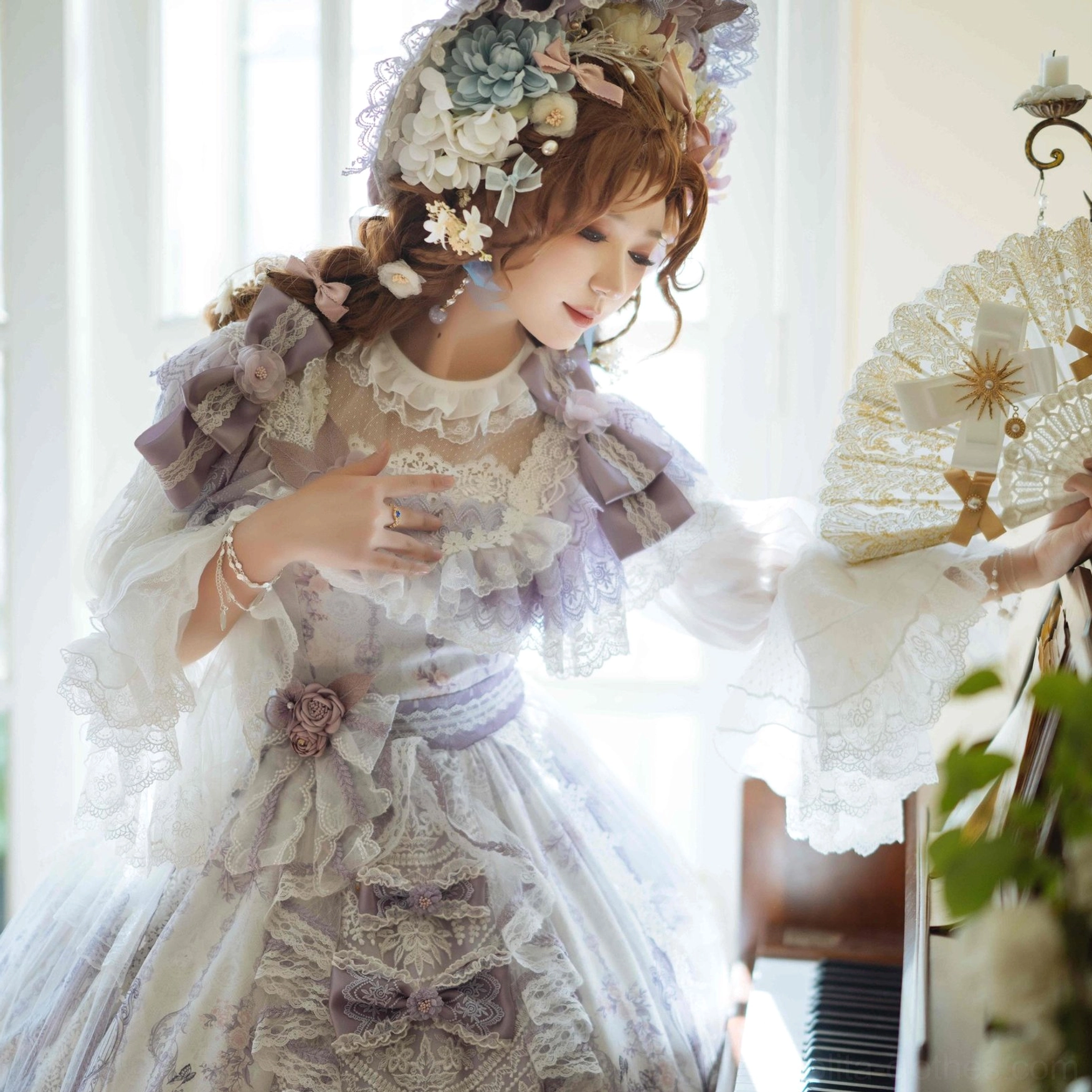 Full vintage Lolita ball gown with purple-cream color scheme ruffled lace neckline and layered tulle skirt worn by model with floral hair accessory in piano room holding vintage fan