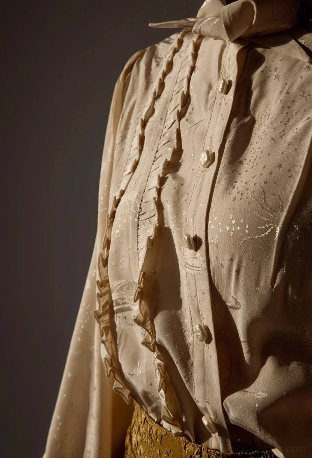 Close-up detail of vintage Lolita blouse front placket showing ruffled trim round pearl buttons warm beige tone with subtle dark floral embossed fabric patterns