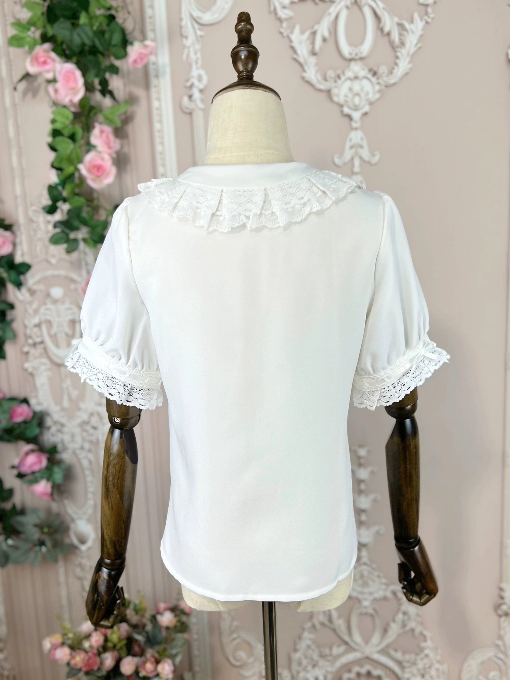 Lolita blouse from rear side perspective showing shirt hem detail back collar lace trim and lace sleeve cuffs against vintage rose vine floral backdrop