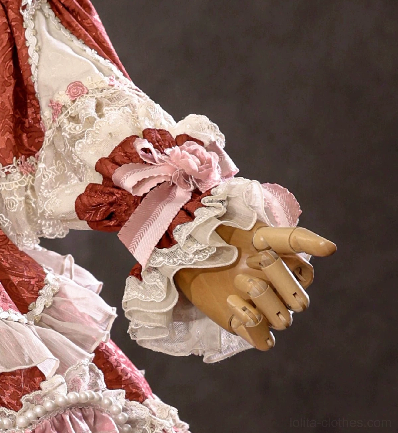 Burgundy red lolita wrist cuff with white ruffled lace, pink satin bow, and fabric rose decoration on wooden mannequin hand