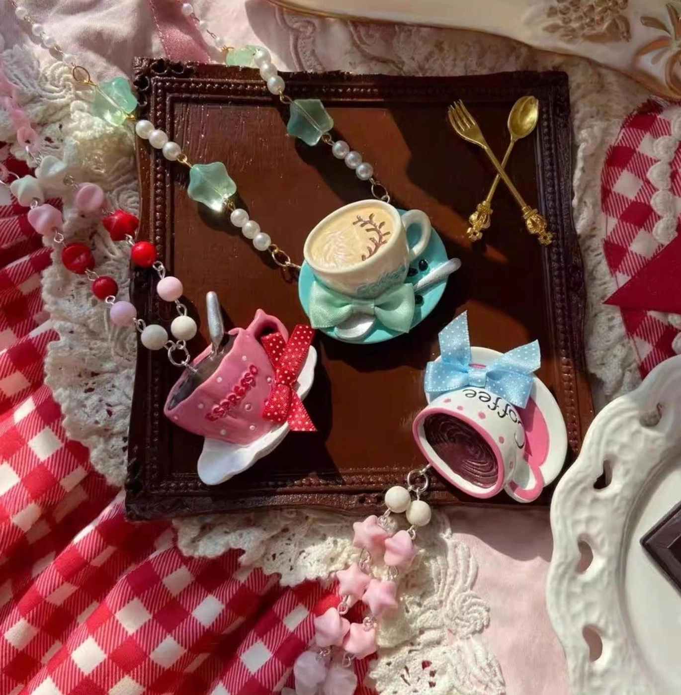Old School Lolita beaded necklace with colorful coffee cup pendants displayed on red gingham fabric with lace and vintage golden tableware in overhead flat lay view