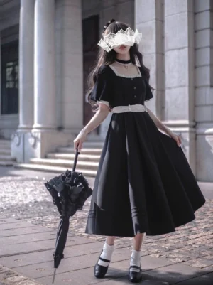 Black vintage Lolita OP dress back view featuring removable white bow sash and ruffled ankle socks, model wearing lace veil and holding black lace umbrella in European stone courtyard setting
