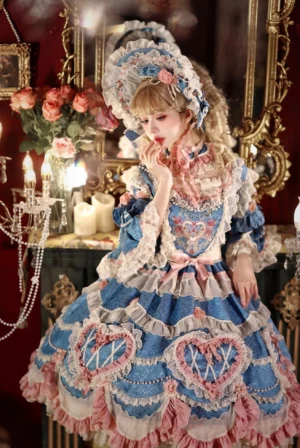 Blue-pink vintage Lolita OP dress with heart embroidery and ruffled lace hem, three-quarter front view in luxury boudoir setting with crystal candelabra and vanity mirror, featuring matching lace bonnet and accessories