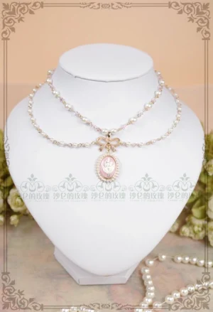 Vintage pearl cameo lolita necklace in classic pink displayed on white jewelry mannequin with green floral decorations, double-layer pearl chain with gold bow charm