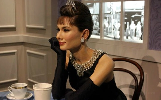 Audrey Hepburn vintage style styling on female model wearing black evening gown with long gloves, pearl tiered choker necklace, matching pearl drop earrings, elegant retro cafe setting