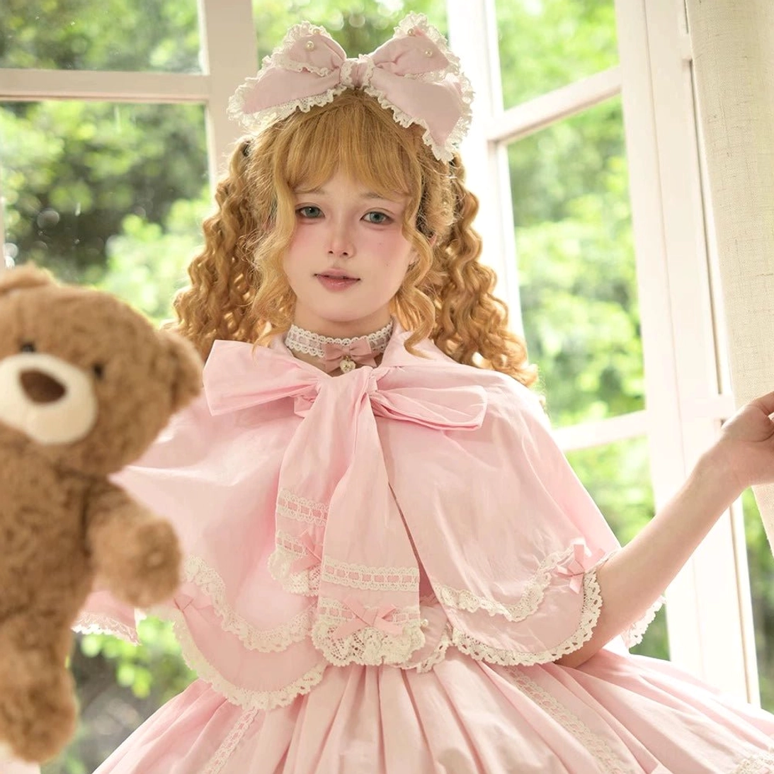 Pink sweet Lolita cape dress with oversized front bow, lace-trimmed capelet, matching head bow and vintage petal rabbit theme close-up