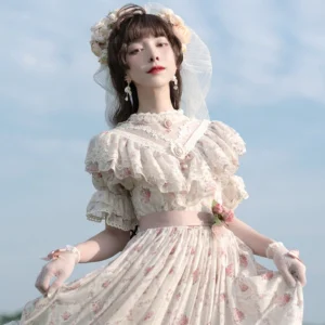 Vintage rose garden floral lolita OP dress with cream base and pink rose prints, featuring ruffled high collar, short puff sleeves with lace trim, satin waist bow, and layered ruffled skirt hem worn by model outdoors