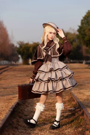 Blonde model wearing complete vintage striped peppy sailor Lolita JSK coordinate with matching cape, structured sailor collar, and coordinating sailor hat at outdoor railway track setting, featuring ruffled socks and vintage leather suitcase styling