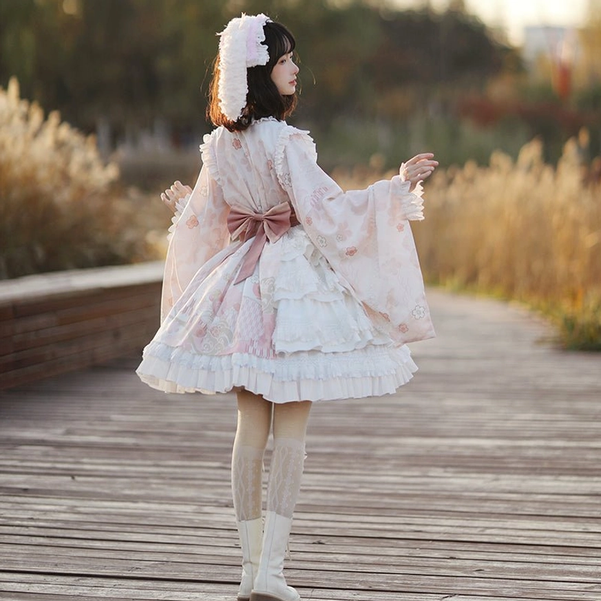 Wa Lolita OP dress back view showing large pink back bow sash and layered ruffled skirt, model standing on wooden boardwalk wearing wide Japanese sleeves and white knee-high stockings