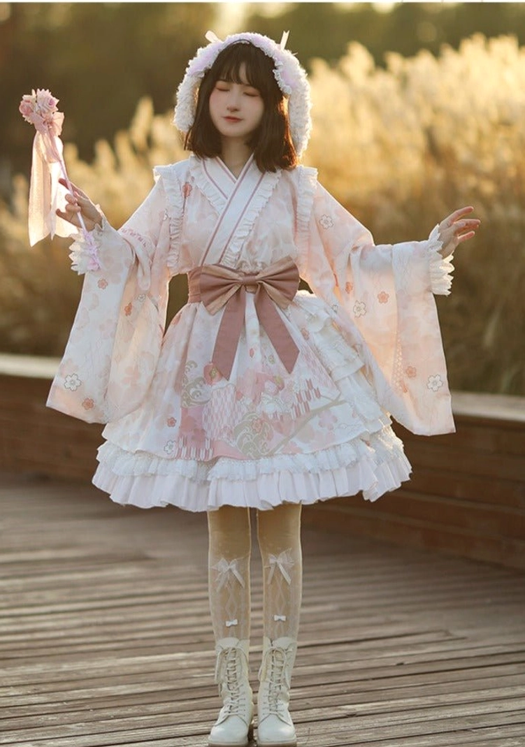 Wa Lolita OP dress in pink cherry blossom print with pink waist sash and rabbit ear hood accessory, full front body view with model holding pink floral wand in sunset reed field and white lace boots