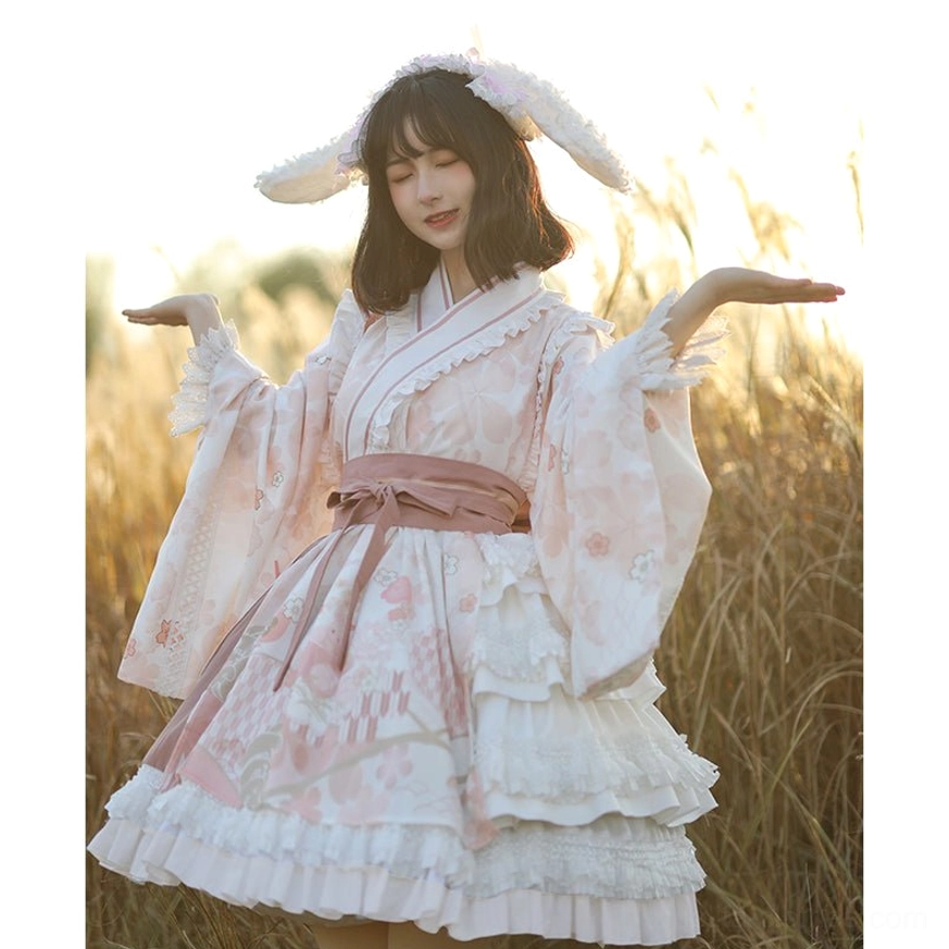 Wa Lolita OP dress in cherry blossom pink and white with rabbit ear hair clips, front full body view on model wearing pink waist sash and layered ruffled skirt in sunset reed field setting