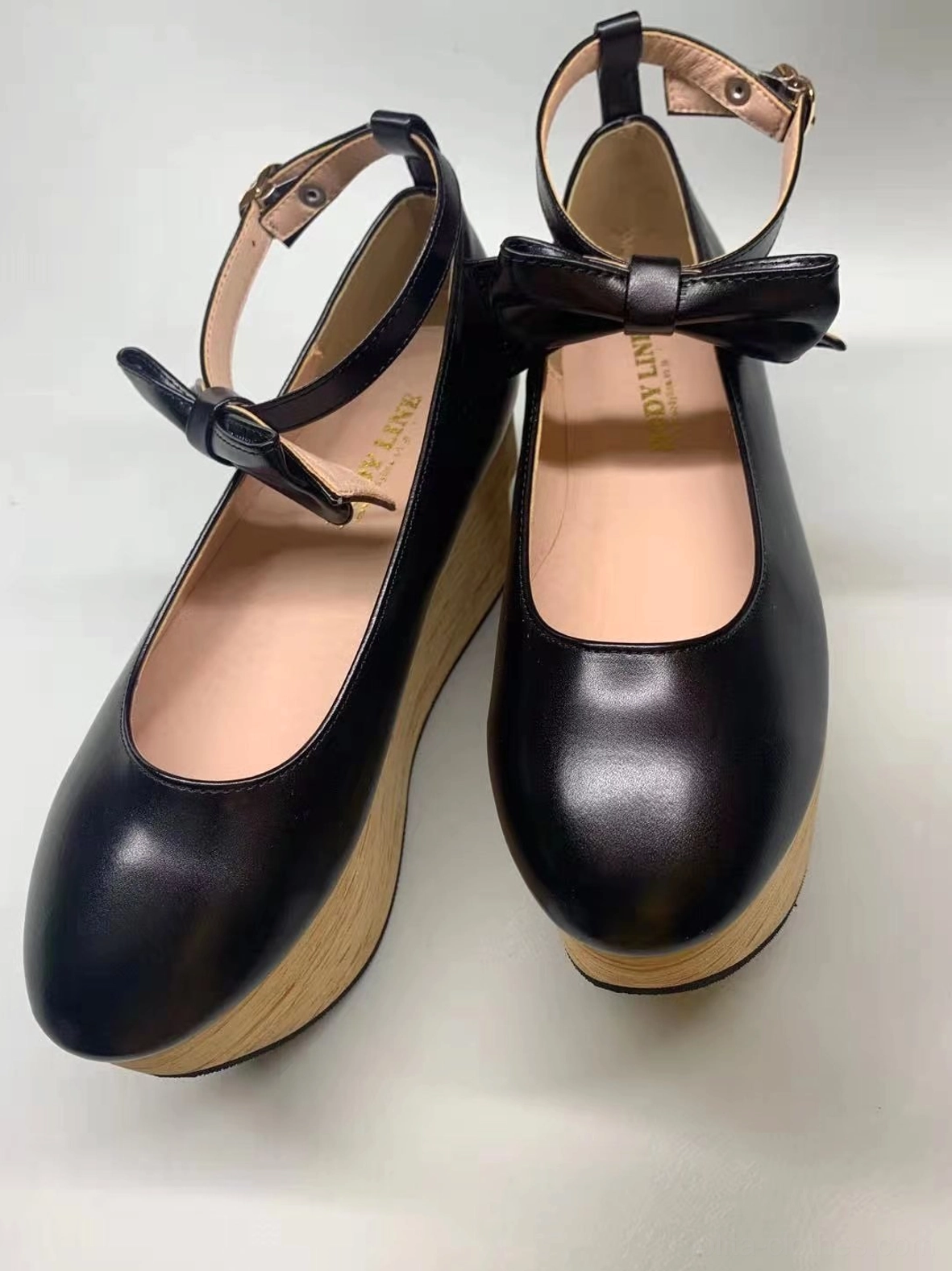 Black glossy patent leather wa lolita platform Mary Jane shoes with round closed toe, adjustable ankle buckle strap, decorative satin bow, and authentic wood-grain wedge platform heel, front flat lay view on light background