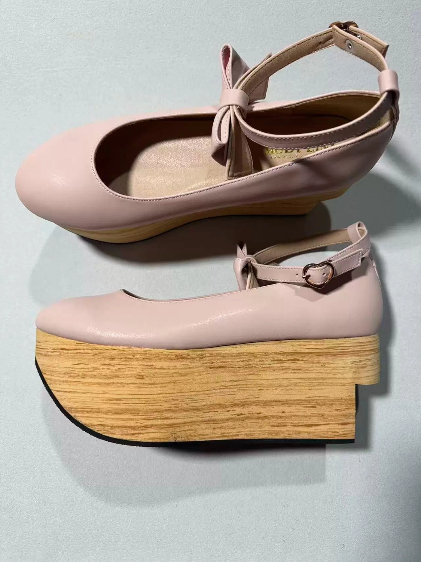 Nude pink wa lolita platform Mary Jane shoes with round closed toe, ankle strap featuring bow and buckle decoration, smooth leather upper, thick simulated wood-grain wedge platform heel, shown in frontal flat lay and side profile on plain dark gray background
