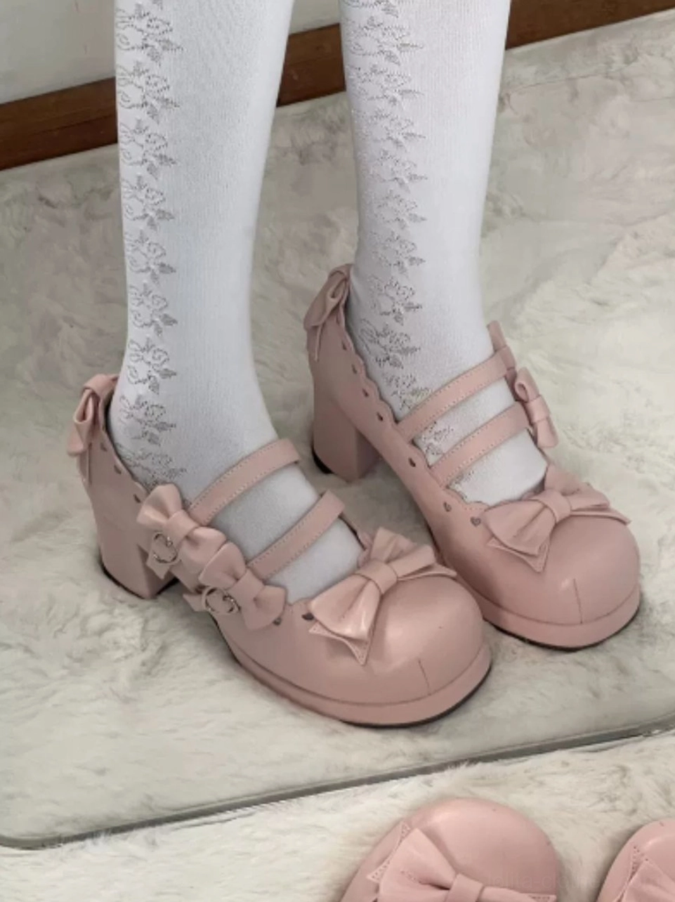 First-person foot wear view of pink wa lolita platform Mary Jane shoes with round toe, ankle strap with decorative bow ornament, authentic wood-grain wedge platform heel, styled with white floral lace thigh-high socks on indoor home floor background