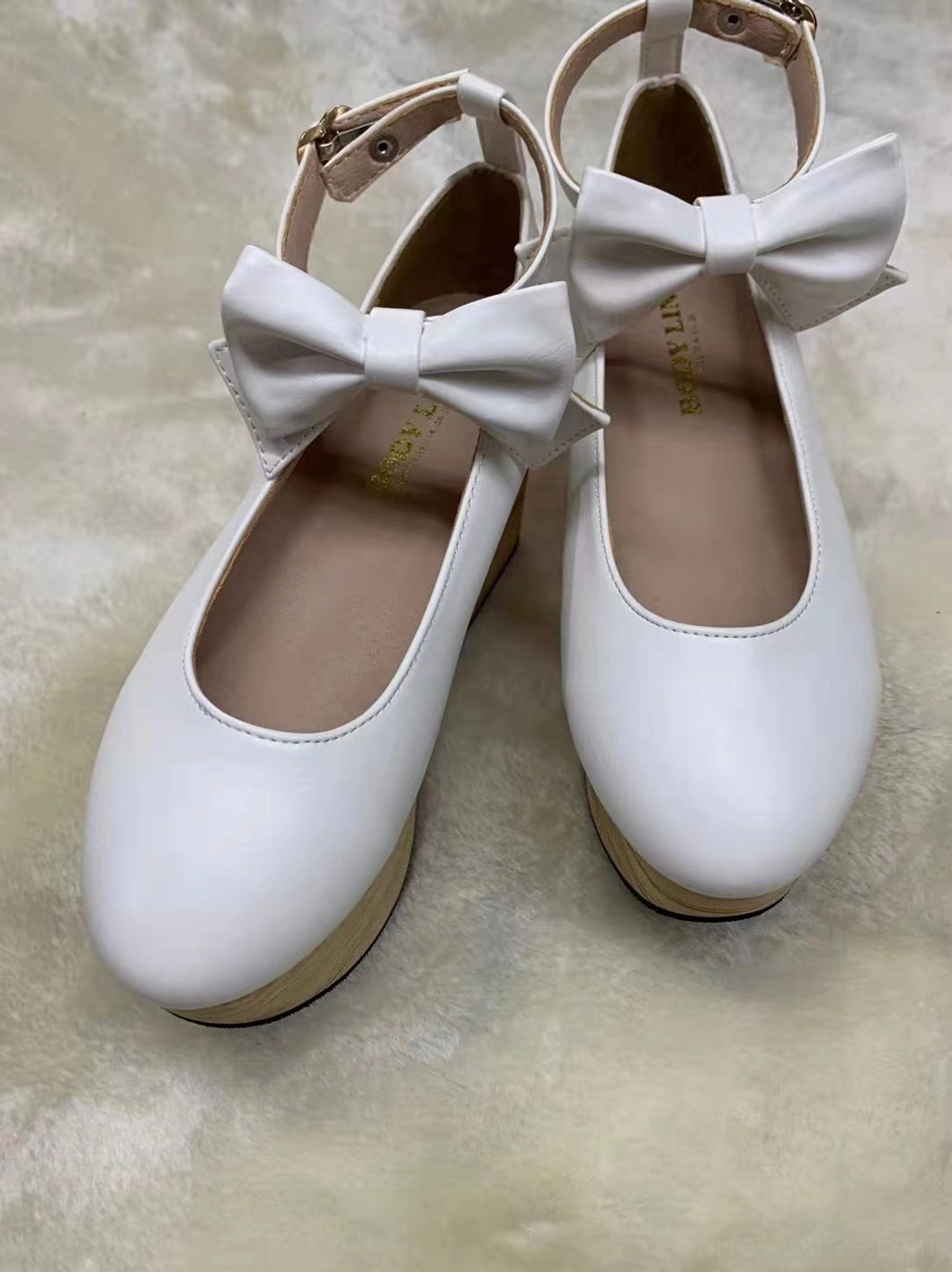 White wa lolita platform Mary Jane shoes with large decorative satin bow on ankle strap, round closed toe, smooth leather upper, and prominent wood-grain thick wedge platform heel, top-down view on light plush fabric background