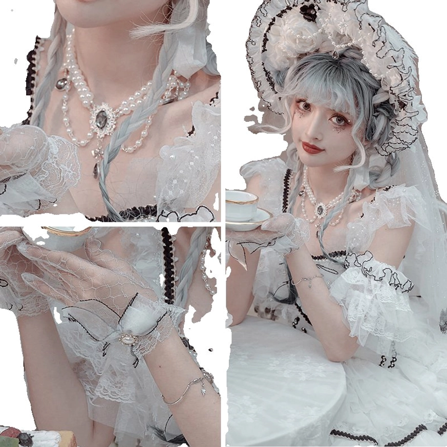 Complete Wedding Lolita bridal accessory ensemble displayed on seated model at outdoor white tea table in afternoon tea setting, showing bonnet with veil, multi-strand pearl necklace, mesh gloves, and full ruffled black-trimmed lace gown as coordinated set