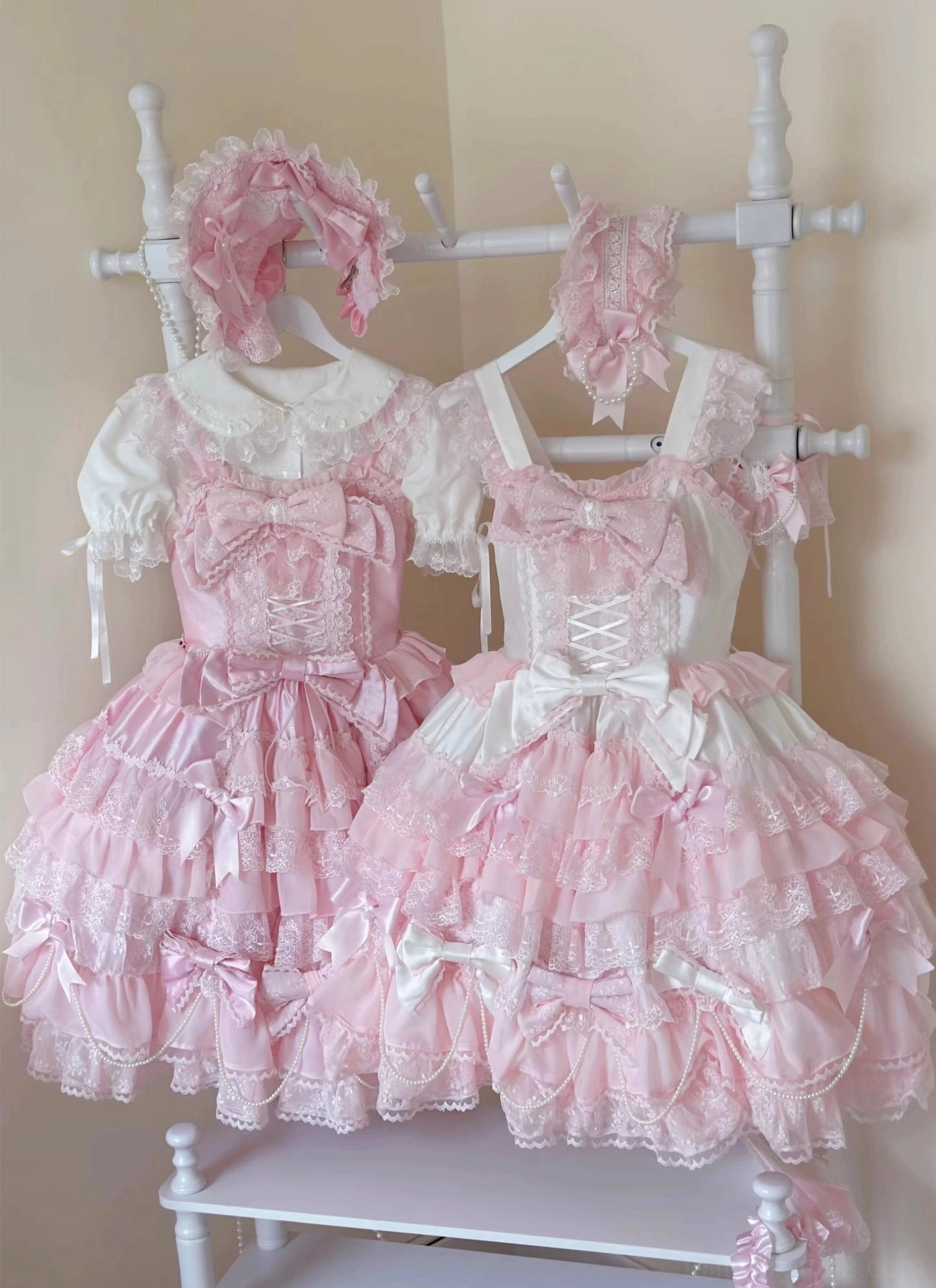 Overhead flat lay of two complete pink and white wedding lolita outfit sets with matching hairstyles headbows and accessories showing tiered ruffled skirts and lace trim details