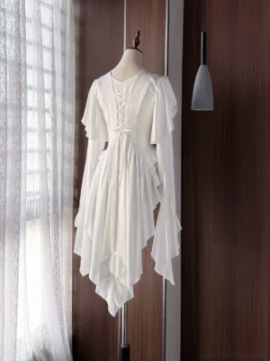 White asymmetric Ouji Lolita dress ensemble front full shot on dress mannequin displaying lace-up corset back, flowing irregular fishtail hem, flared long sleeves, studio setting with wood wall backdrop