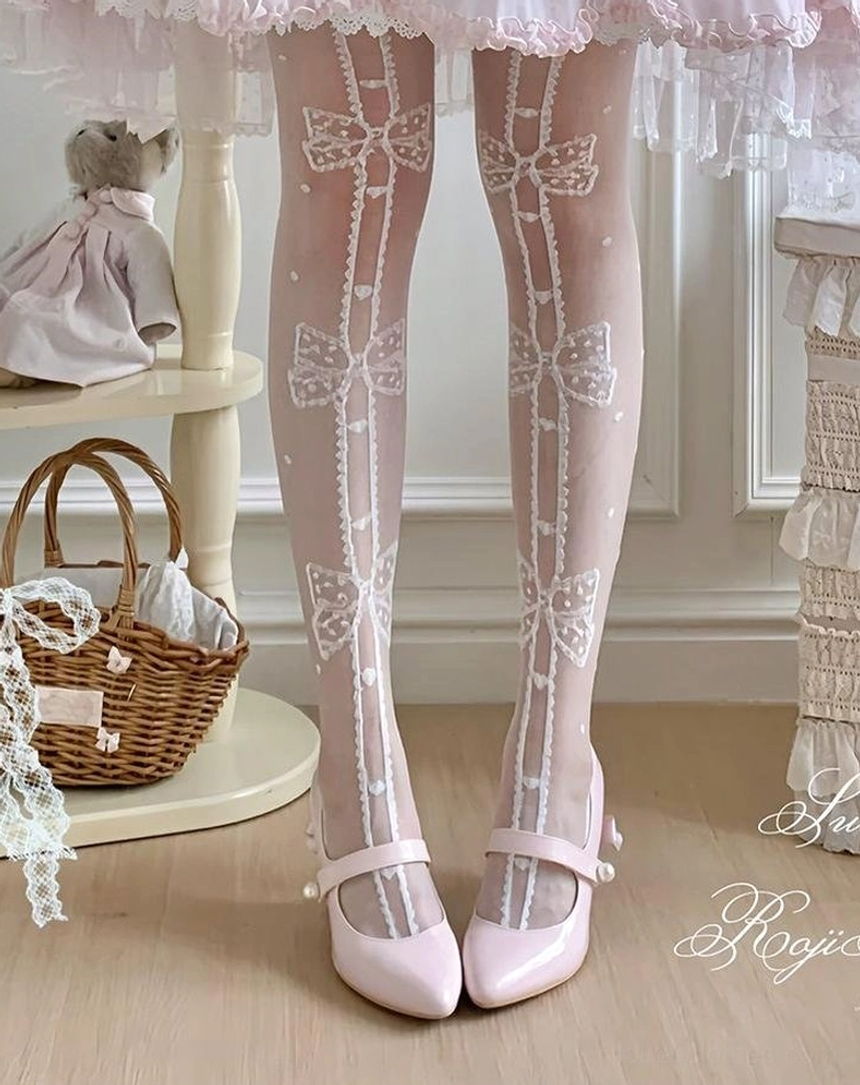 White sheer sweet lolita thigh-high socks with vertical bow and polka dot print close-up front leg view worn with pink frilly lolita skirt and pink mary jane flats showing clear pattern definition and lace cuff trim