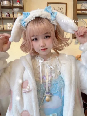 Fluffy white lop-eared bunny sweet lolita hairband with black bow brooch worn by blonde girl in cozy cafe setting - front close-up portrait view