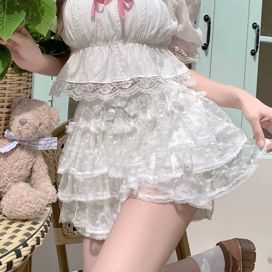 White cake-style ruffled Lolita shorts with multi-layered ruffled hem and soft lace cotton fabric worn by seated model in low-angle side view with teddy bear