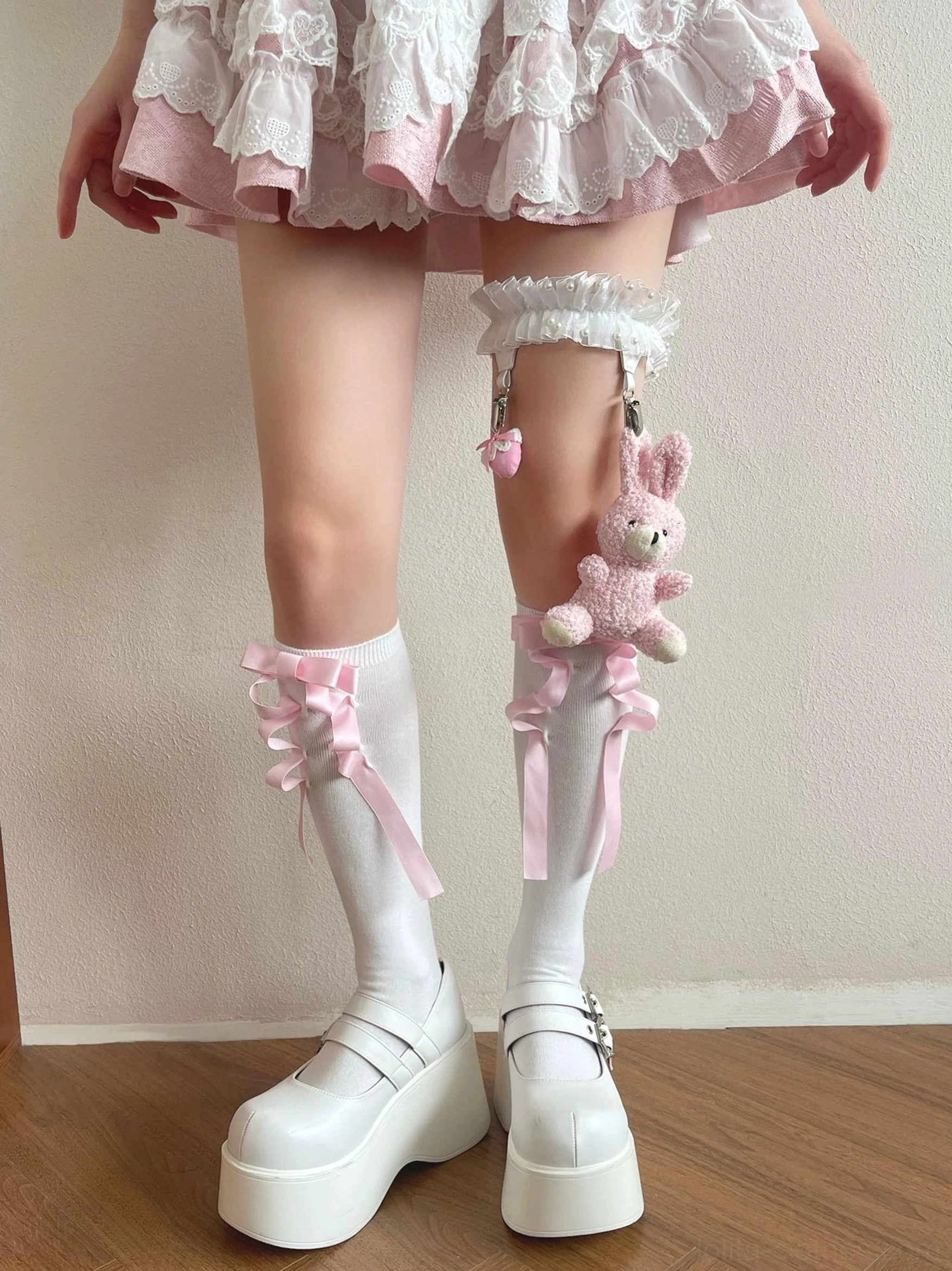 White calf socks with pink ribbon bow accents and matching doll leg garter featuring ruffled lace trim and detachable plush bunny charm from front low-angle close view