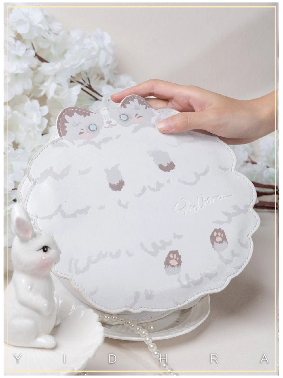 White ragdoll kawaii cat leather shoulder bag front close-up held by hand with cherry blossom and rabbit ornaments, showing soft embroidery and scalloped surface