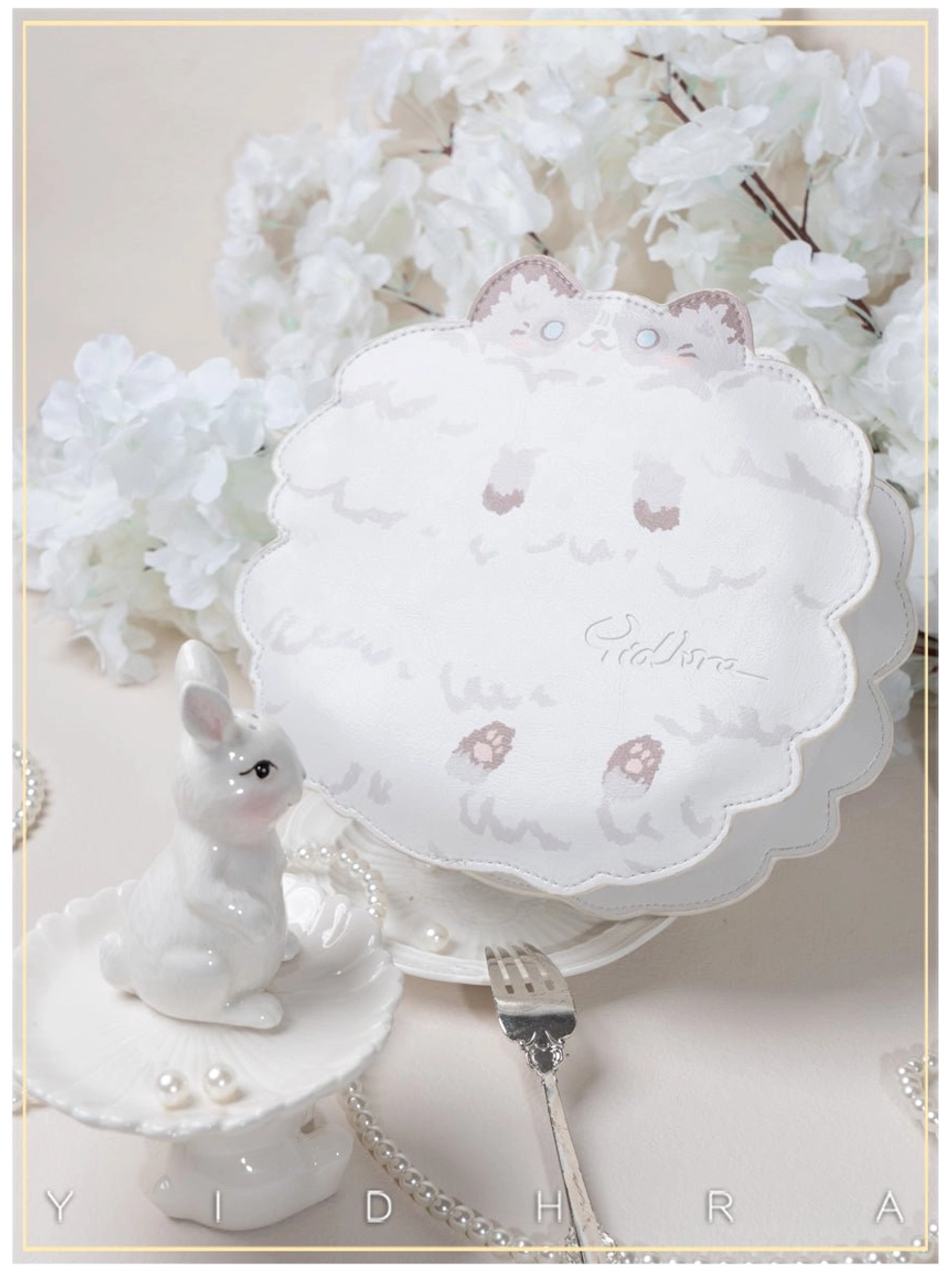 White kawaii cat leather shoulder bag oblique top-down tabletop view with elegant cat-themed prints and scalloped round shape on porcelain backdrop