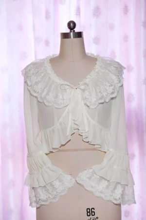 White sheer chiffon Lolita cropped blouse featuring ruffled doll collar with self-tie bow detail and lace-trimmed cuffs and hem, front view on dress form with pink curtain backdrop
