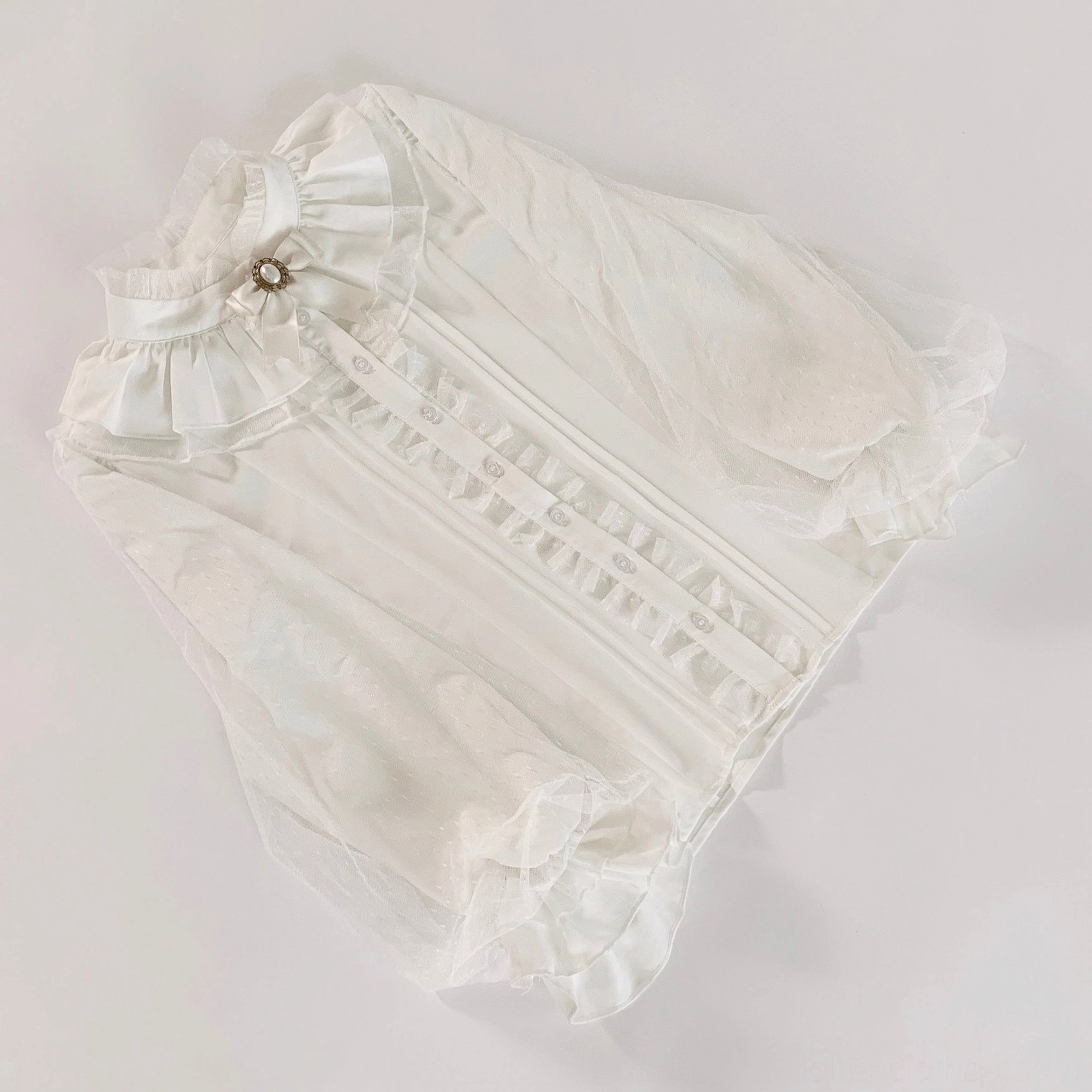 White chiffon lolita inner blouse flat lay with ruffled stand collar lace pleated placket and sheer ruffled cuffs detail