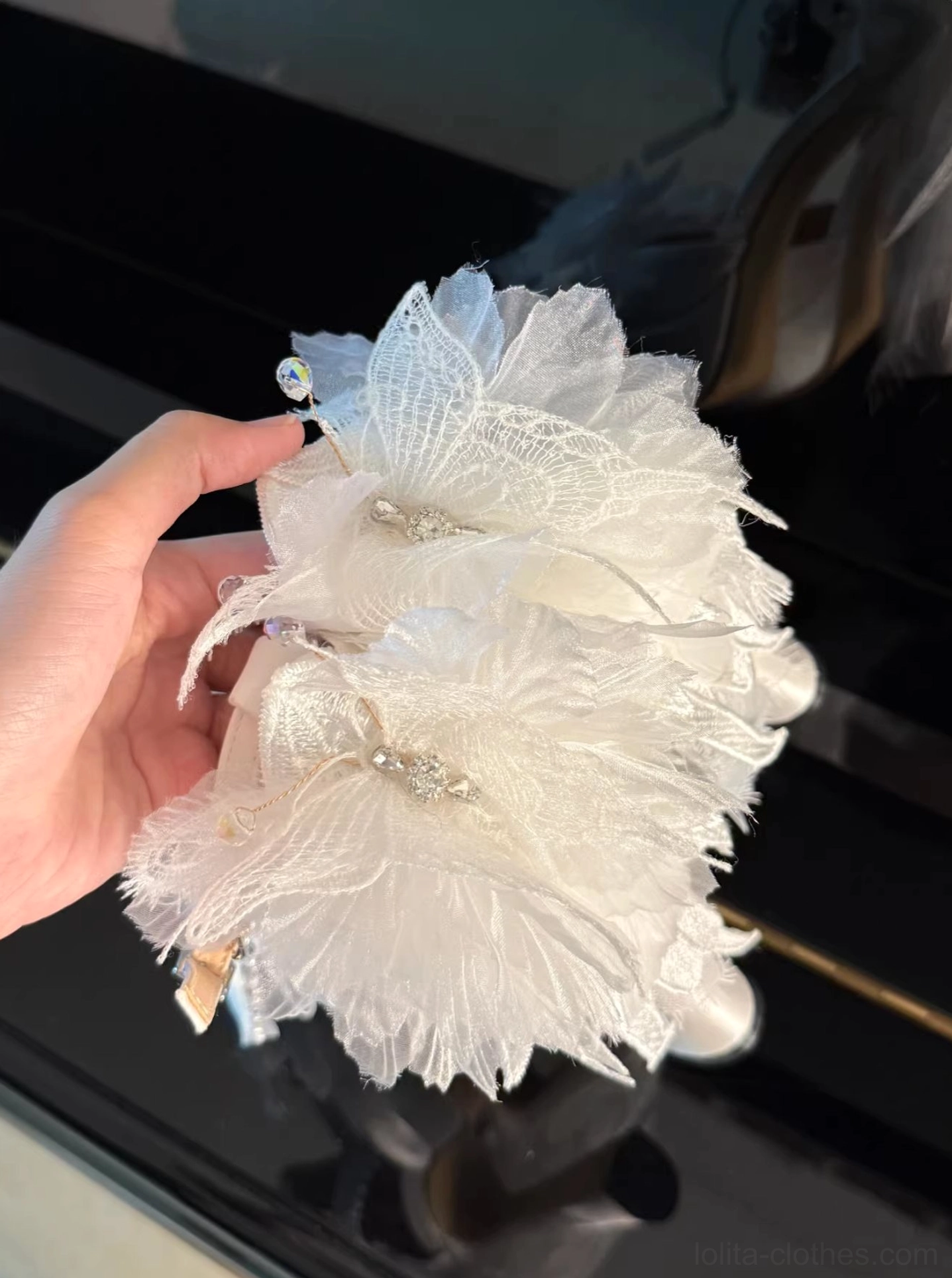 White feather flower lolita shoe accessories and decorative embellishments featuring fluffy feathers, lace mesh petals, and rhinestone gem decorations, close-up hand-held prop shot