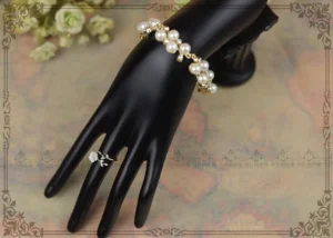 White flower Classical Lolita ring styled on a hand with coordinating pearl bracelet against a vintage floral background