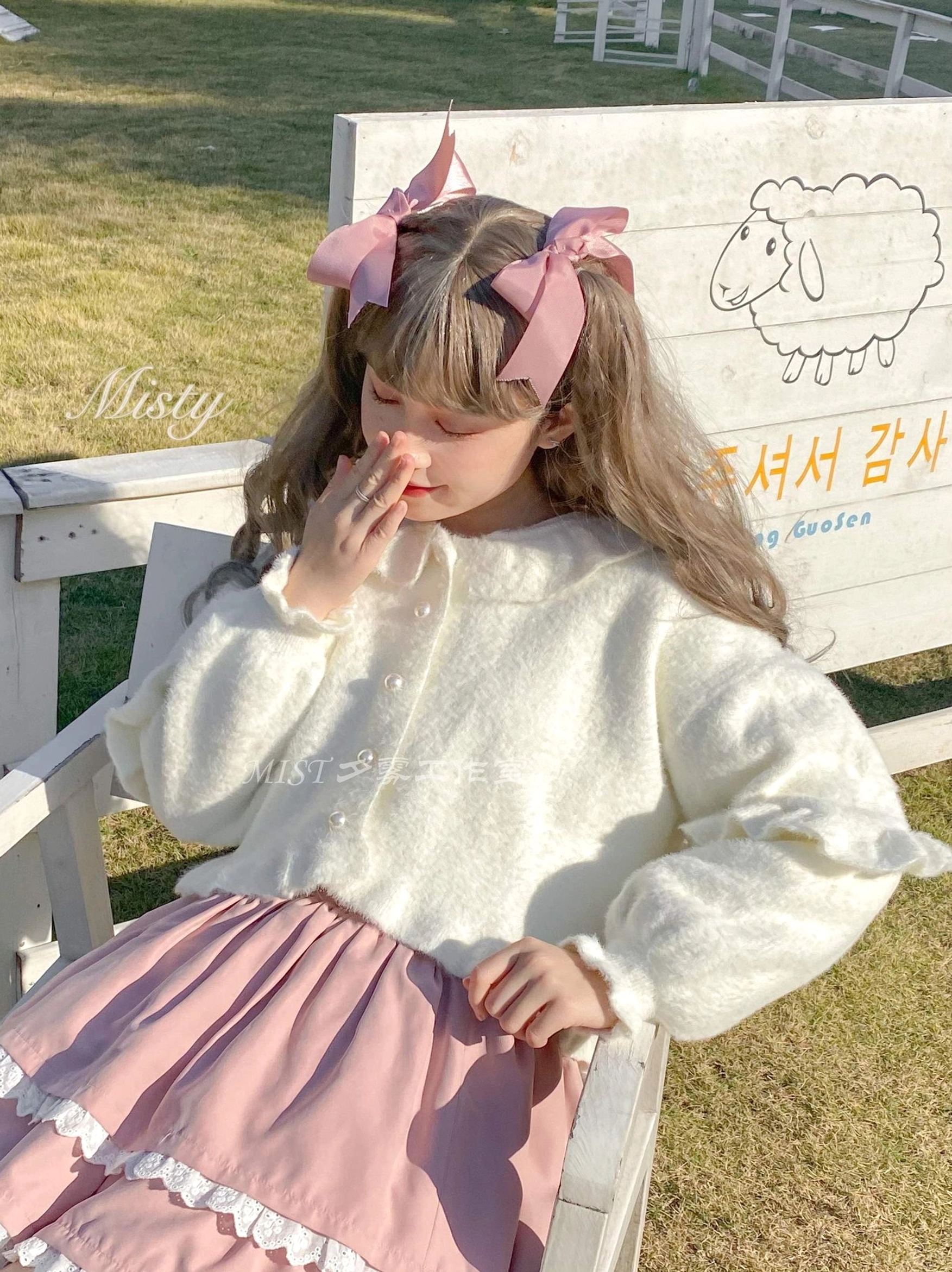 White fluffy lolita cardigan pink ruffle skirt seated front view doll collar puff sleeves pearl buttons outdoor wooden fence scene