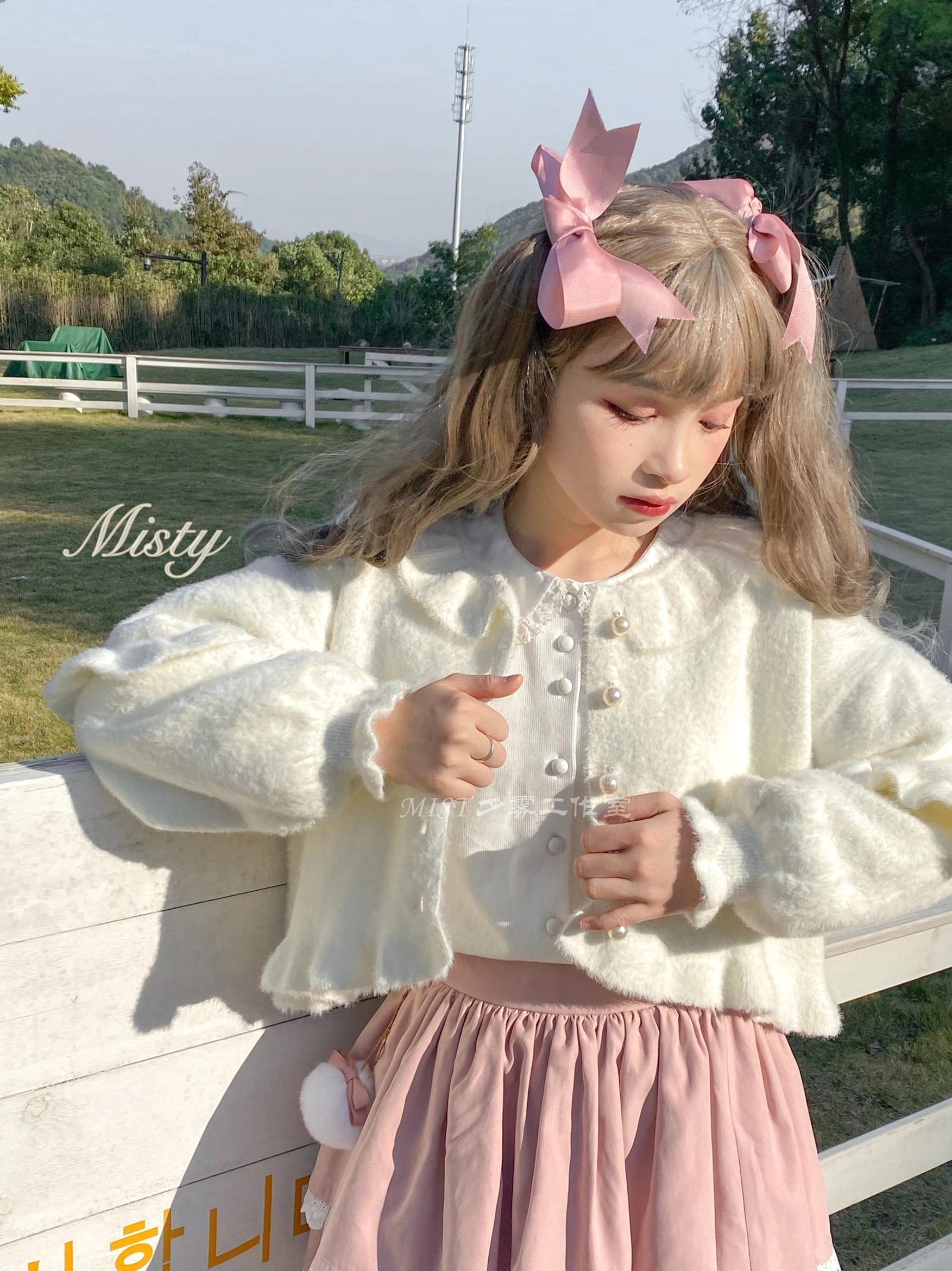 White fluffy sweet lolita cardigan pink ruffled skirt set three-quarter side view girl adjusting outfit outdoor ranch setting