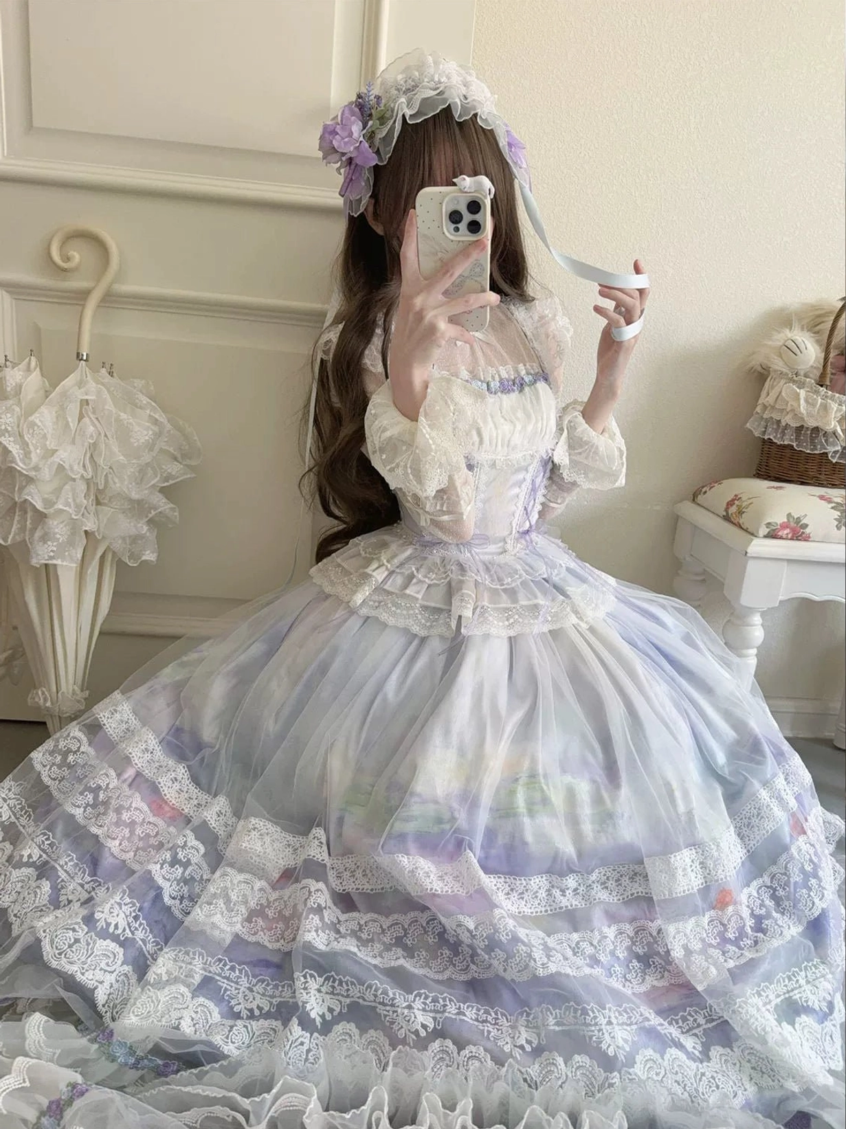 White classic lolita ballgown dress with multiple lace layers on voluminous full skirt, ruffled bodice, and flower hair accessory, low-angle indoor selfie view