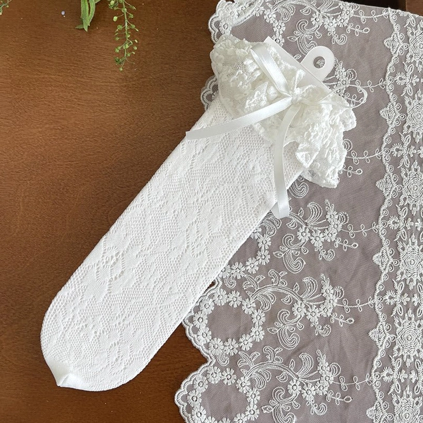 Single off-white French Lolita mid-calf lace sock overhead flat lay view displaying smooth lace fabric, dainty ruffled bow cuff on embroidered vintage placemat